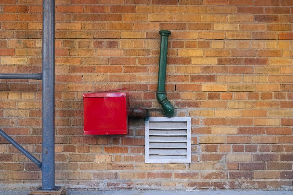 Green pipe and a red box against a brick wall